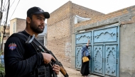 This photograph taken on October 29, 2024 shows an elite police personnel (L) standing guard as a health worker marks houses with numbers during a door-to-door poliovirus vaccination campaign for children on the outskirts of Peshawar. (Photo by Abdul MAJEED / AFP)
