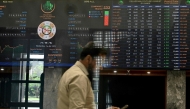 A stockbroker walks past share prices on a financial market board during a trading session at the Pakistan Stock Exchange (PSX) in Karachi on April 9, 2025. (Photo by Rizwan TABASSUM / AFP)