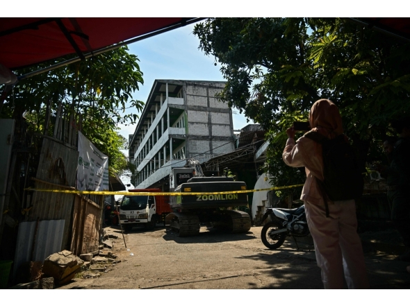 A woman takes a picture in front of the collapsed Al Khoziny Islamic boarding school in Sidoarjo, East Java, on October 6, 2025, as recovery efforts continue. (Photo by Juni Kriswanto / AFP)