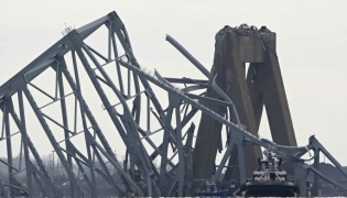 The steel frame of the Francis Scott Key Bridge lies in the water after it collapsed in Baltimore, Maryland, on March 26, 2024. Photo by Mandel NGAN / AFP.

