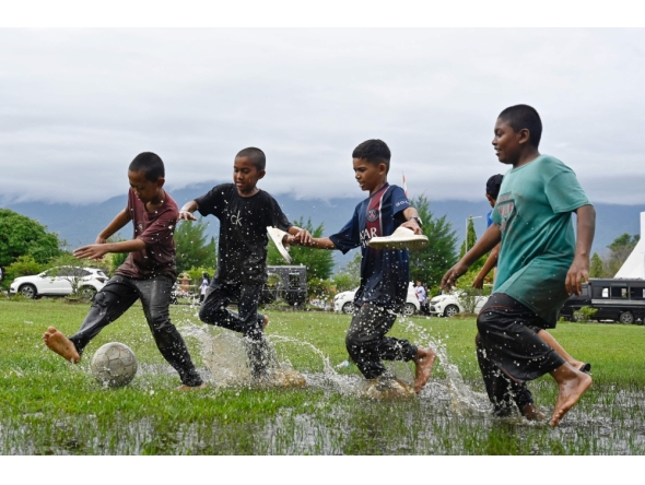 Children play football in a flooded field following rain in Jantho, Aceh province on November 24, 2025. (Photo by Chaideer Mahyuddin / AFP)