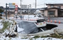 A vehicle rests on the edge of a collapsed road in Tohoku town in Aomori Prefecture on December 9, 2025, following a 7.5 magnitude earthquake off northern Japan. A big quake off northern Japan left at least 30 injured, authorities said on December 9, damaging roads and leaving thousands without power in freezing temperatures. (Photo by JIJI Press / AFP) 
