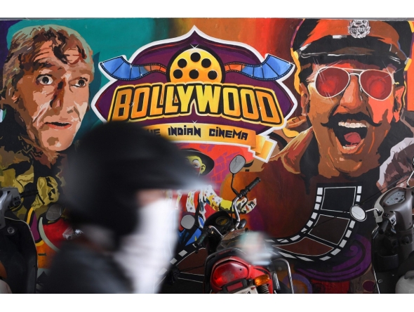 A motorist rides past a wall mural with images of Bollywood actors in Mumbai on June 29, 2020. Photo by Indranil MUKHERJEE / AFP