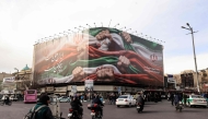 Vehicles pass by a large patriotic banner depicting the Iranian flag in Tehran on January 14, 2026. (Photo by Atta Kenare / AFP)