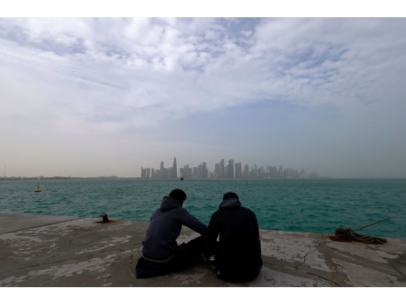 Visitors sit along the waterfront on a foggy day at the Corniche area facing the high-rise buildings in the West Bay district, in Doha on January 15, 2026. (Photo by Karim JAAFAR / AFP)
