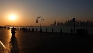 A man is silhouetted by the setting sun as he rides his motorcycle in Doha's Mina district on February 26, 2026. (Photo by Karim Jaafar / AFP)