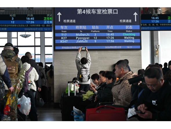 A man takes pictures of a board with a sign for the K27 train bound for Pyongyang as passengers wait for their train at Beijing Railway Station in Beijing on March 12, 2026. The first passenger train service from North Korea to China crossed the border March 12 for the first time in six years, Yonhap News Agency reported. (Photo by Adel Berry/ AFP)
 