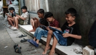 Children play online games against each other on smartphones and tablets along an alley in Jakarta on March 26, 2026. Photo by YASUYOSHI CHIBA / AFP