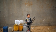 A displaced Palestinian boy stands on a trolley loaded with empty water canisters at the Nuseirat refugee camp, in the central Gaza Strip on April 1, 2026. (Photo by Eyad Baba / AFP)