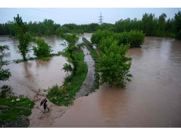 A man walks along a flooded path as torrential rains cause water channels to overflow, inundating nearby areas of Peshawar on April 7, 2026. Photo by Abdul MAJEED / AFP