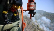 A Thai Department of Disaster Prevention and Mitigation (DDPM) personnel on a firefighting helicopter inspects fire spots to drop water to combat forest fires over Mae On district in the northern Thai province of Chiang Mai on March 26, 2025. Photo by MANAN VATSYAYANA / AFP