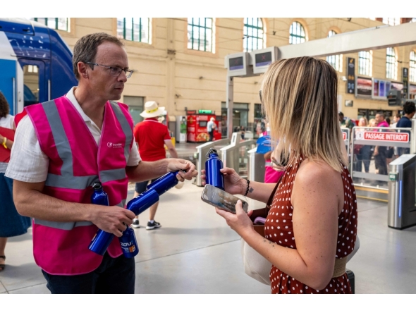 A staff member hands out flasks to customers as part of a distribution of water bottles, hats and fans at the Saint-Charles railway station in Marseille on June 22, 2026. (Photo by Miguel Medina / AFP)