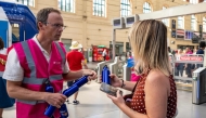 A staff member hands out flasks to customers as part of a distribution of water bottles, hats and fans at the Saint-Charles railway station in Marseille on June 22, 2026. (Photo by Miguel Medina / AFP)