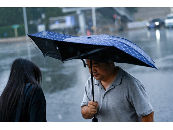 A man holding an umbrella walks along a road on a rainy day in Beijing on July 10, 2026. (Photo by WANG Zhao / AFP)