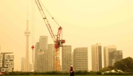A person walks by the skyline of downtown Toronto, as smoke from forest fires in Northern Ontario causes poor air quality over the city, in Toronto, Ontario, Canada, Wednesday, July 15, 2026. (Photo by Cole BURSTON / AFP)