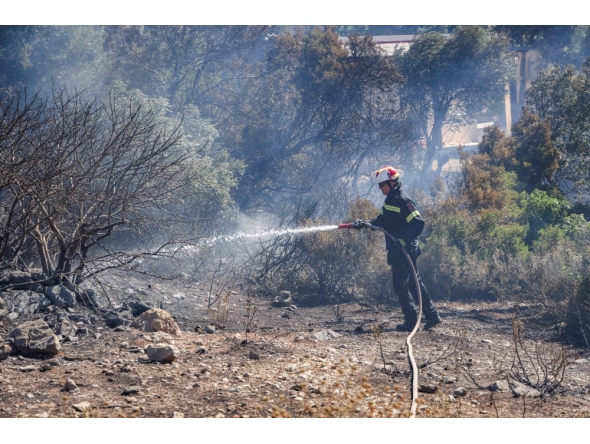 A firefighter uses a waterhose as he works to battle a wildfire, south of Rethymno in the Greek island of Crete on July 30, 2026.(Photo by Costas METAXAKIS / AFP)