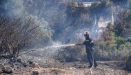 A firefighter uses a waterhose as he works to battle a wildfire, south of Rethymno in the Greek island of Crete on July 30, 2026.(Photo by Costas METAXAKIS / AFP)