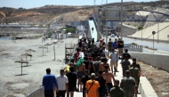 A group of migrants approach the border post to make their way back to Morocco, escorted by Spanish infantry soldiers, in the Spain's north African enclave of Ceuta, on August 2, 2026. (Photo by Henry Nicholls / AFP)