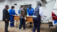 Takemore Malunga (L) watches as pallbearers carry the coffin of his maternal uncle, a victim of the capsized passenger ferry, at the Kariba Hospital mortuary in Kariba, on August 14, 2026. (Photo by Jekesai NJIKIZANA / AFP)