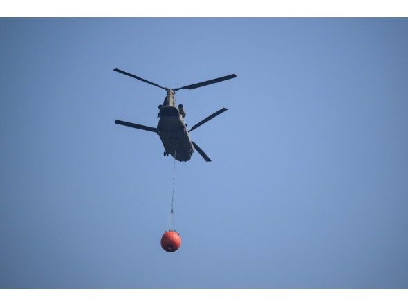 A Royal Netherlands Air Force Boeing CH-47D Chinook carrying a bambi bucket departs from Baelen, near Eupen, eastern Belgium to tackle a wildfire burning in the Hautes Fagnes (High Fens) nature reserve on August 16, 2026. Photo by JOHN THYS / AFP