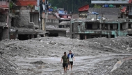Flash flood survivors walk through sludge past damaged houses searching for salvageable belongings at Trishuli Center in Nepal's Nuwakot district on August 30, 2026. Photo by Arun SANKAR / AFP