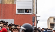 A resident watches from her window migrants waiting on the sidewalk before being registered in Loma Colmenar district of Ceuta on August 31, 2026. Photo by Antonio Sempere / AFP