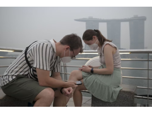 Tourists wear protective masks while seated across Marina Bay Sands in Singapore on October 15, 2026, as the country continues to be shrouded in haze caused by fires in Indonesia / AFP