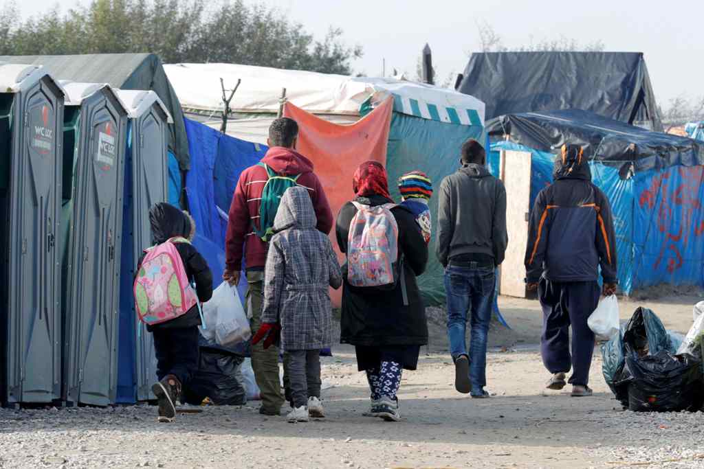 Migrants carry their belongings as they walk in an alley near tents and makeshift shelters on the eve of the evacuation and dismantlement of the camp called the 