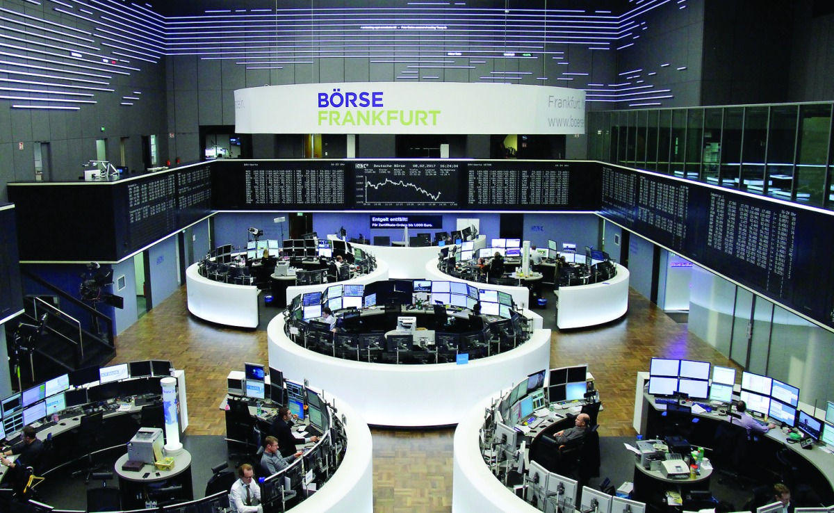 Traders work at their desks in front of the German share price index, DAX board, at the stock exchange in Frankfurt.
