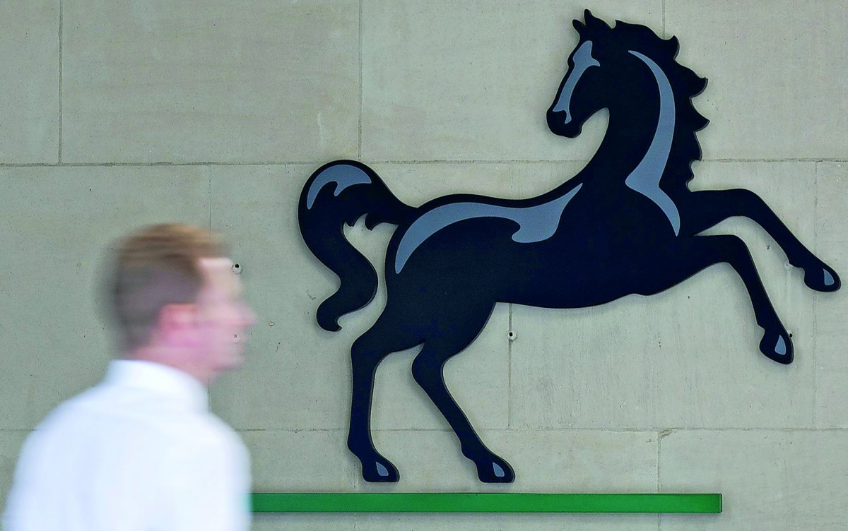 A man passing a Lloyds logo outside the entrance to an office of Lloyds Banking Group in London.