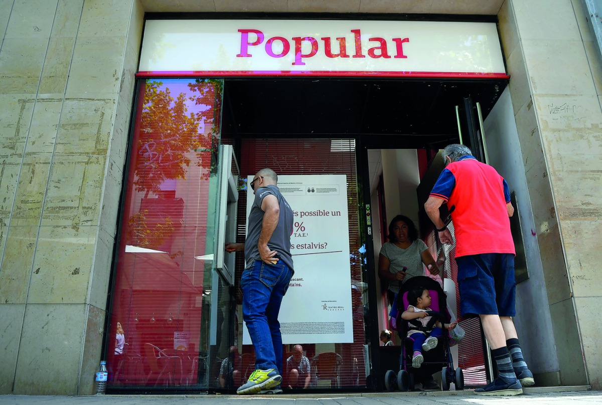 A man operates at the ATM as customers exit a Banco Popular branch, yesterday, near Barcelona after European authorities announced the sale of the bank.