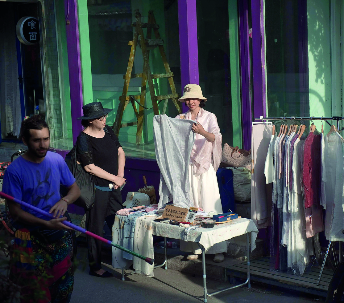 A vendor folds an item as a consumer  looks at other items to be sold on a street while the shop is under construction in Beijing