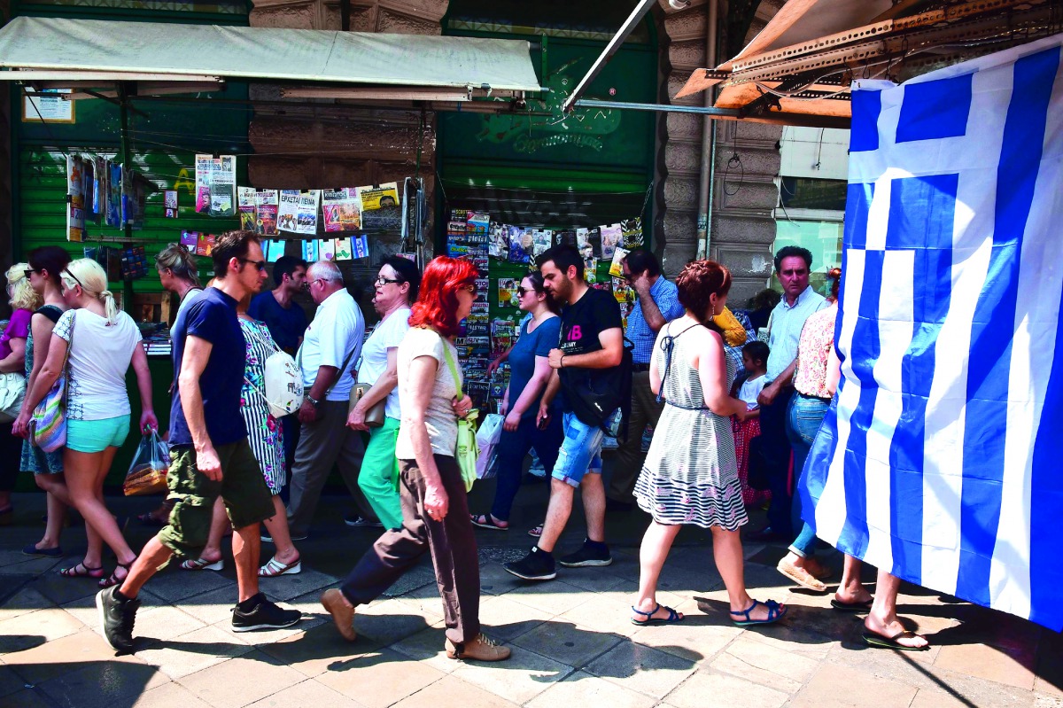 People walk past a Greek flag in central Athens yesterday.   Eurozone ministers struck a long-delayed bailout deal with Greece to unlock badly needed rescue cash.