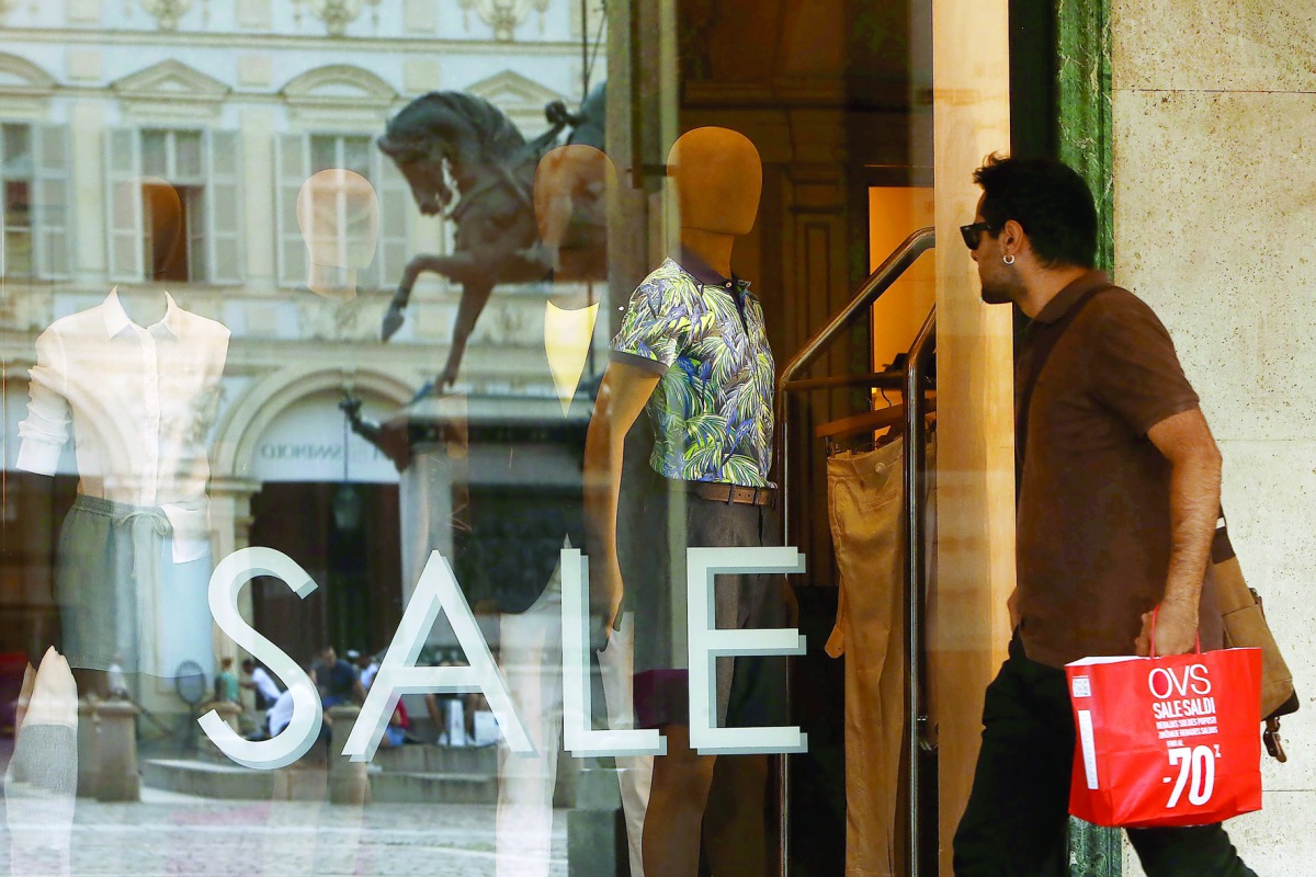 A pedestrian walks by a shop window displaying sales notices in Turin yesterday, as Italian retailers started their summer sales.