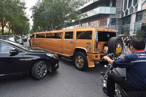 A car and motorcycle wait for a stretched Hummer limousine to go past outside a hotel in Beijing on September 8, 2017. AFP / Greg Baker