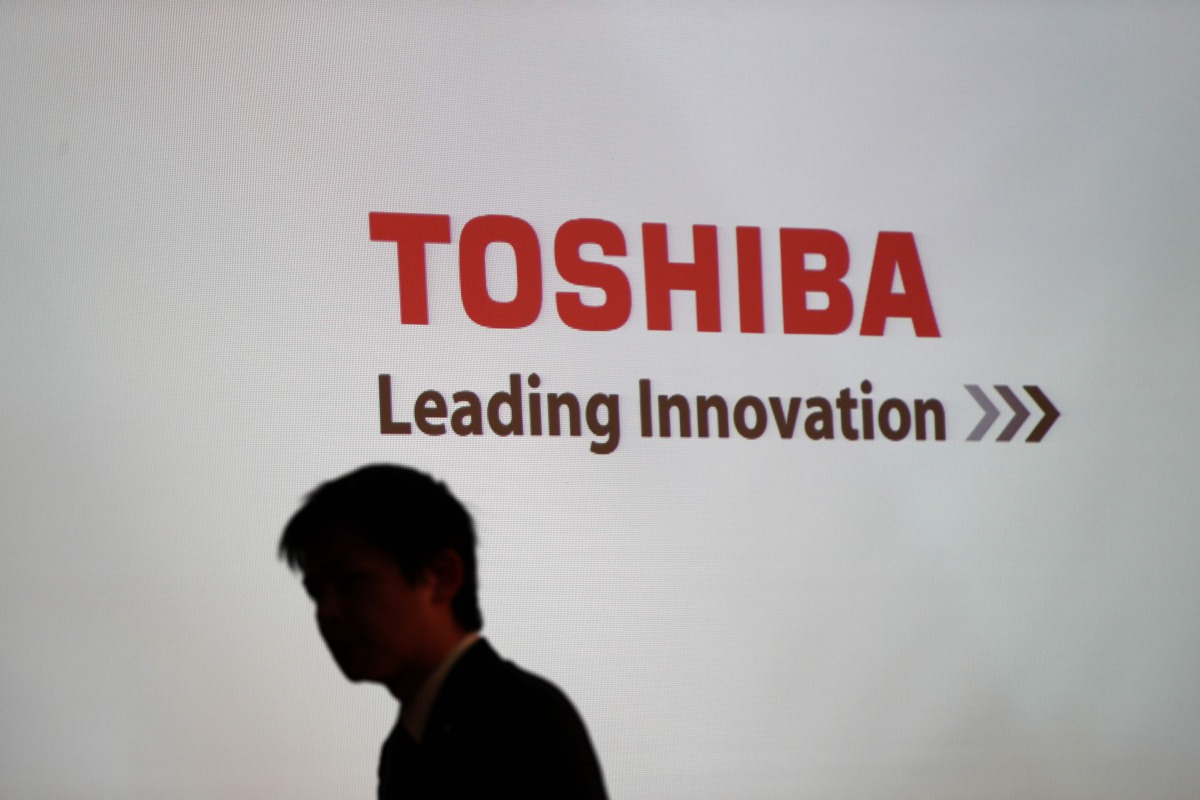 This file photo taken on February 14, 2017 shows  man walking past the logo of Toshiba Corp displayed at the company's headquarters in Tokyo. AFP / Behrouz Mehri
