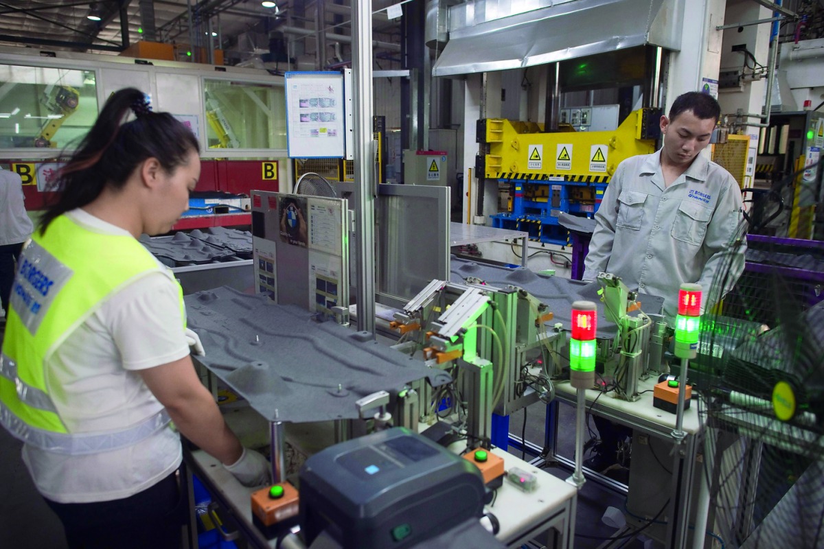 In this picture taken on July 3, 2017 workers manipulate a machine to make car interior pieces for a major European car maker in the American Industrial Park in Shenyang. AFP / Nicolas Asfouri