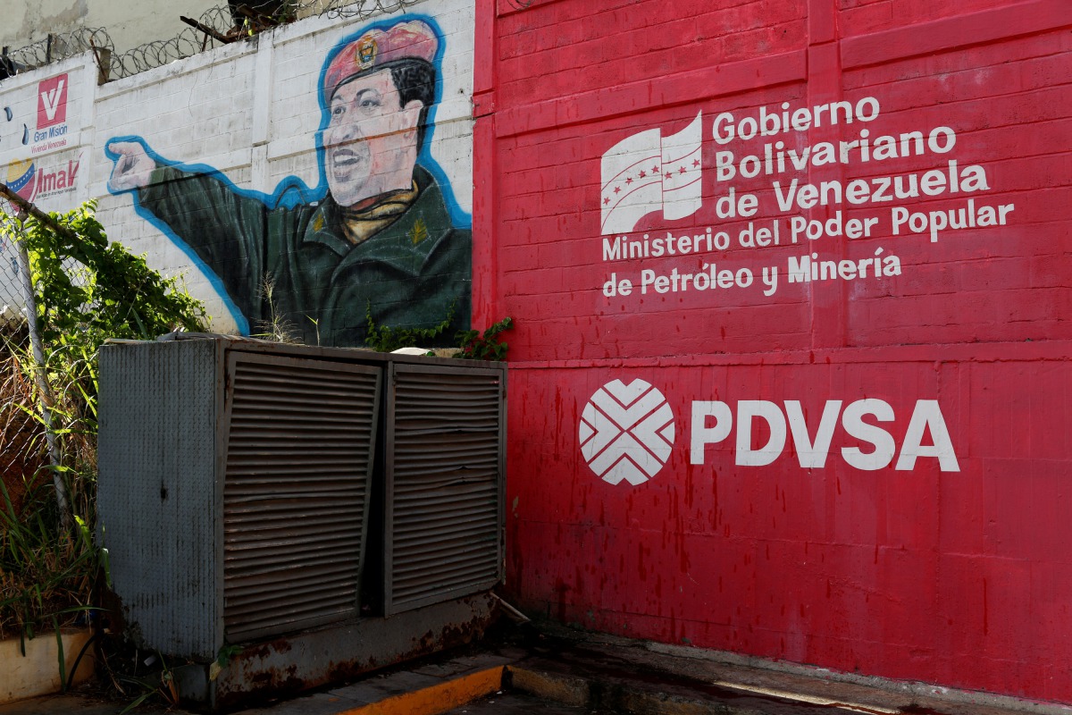 The logo of the Venezuelan state oil company PDVSA is seen next to a mural depicting late President Hugo Chavez at a gas station in Caracas, March 2, 2017 (Reuters / Carlos Garcia Rawlins) 