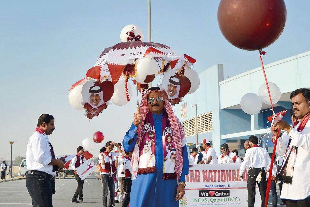 A man holding an umbrella with the pictures of Emir H H Sheikh Tamim bin Hamad Al Thani at Asian Town as part of National Day celebrations. 