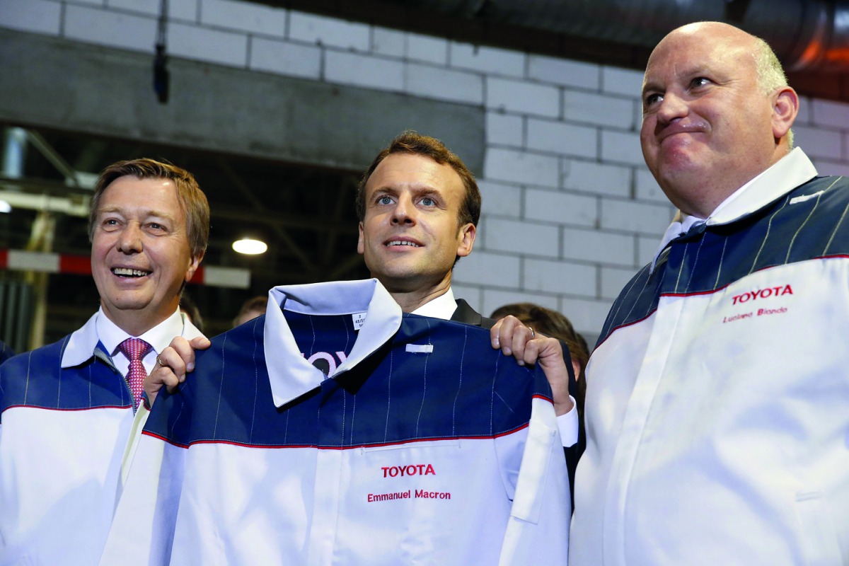 French President Emmanuel Macron (centre) holds a Toyota staff uniform marked with his name as he poses with Toyota Motor Manufacturing France (TMMF) Director Luciano Biondo (right) and Didier Leroy, Executive Vice President of Toyota Motor Corporation, d