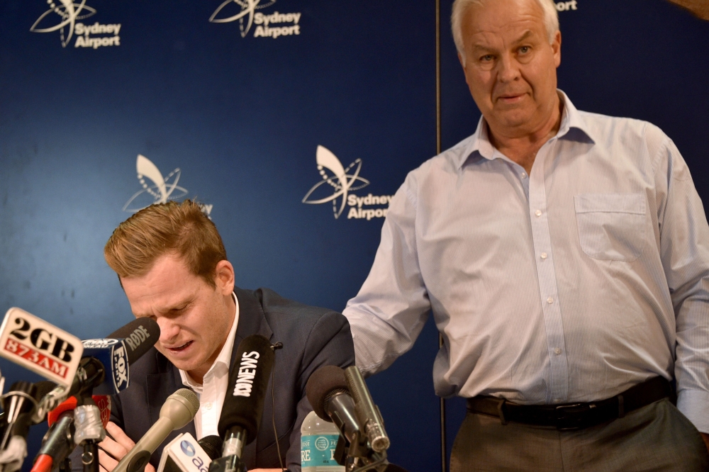 Cricketer Steve Smith (L) is comforted by his father Peter as he reacts at a press conference at the airport in Sydney on March 29, 2018, after returning from South Africa. AFP / PETER PARKS 