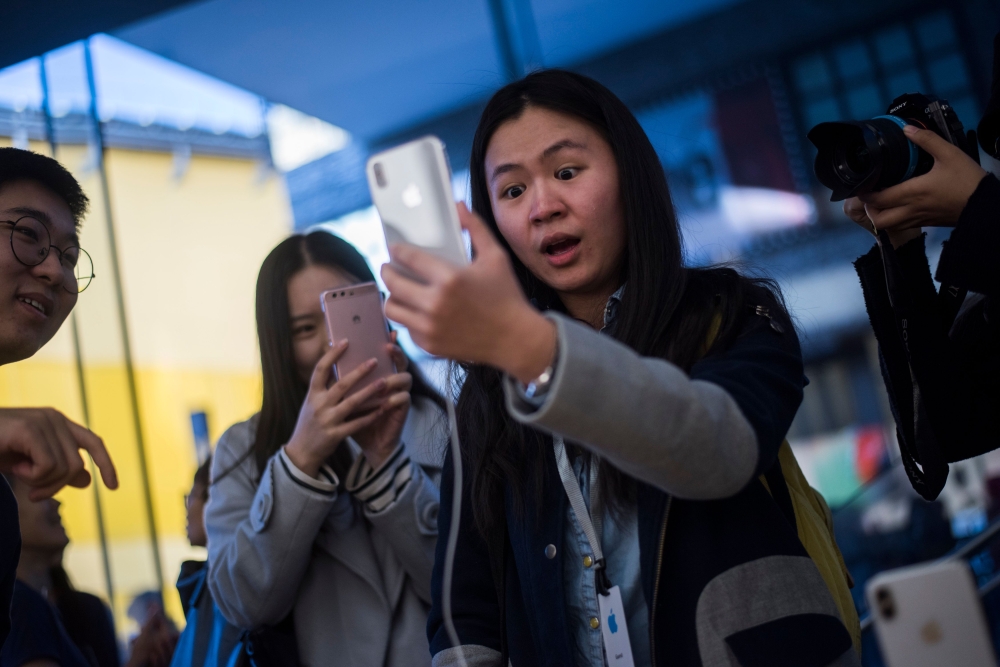 (FILES) A Chinese woman reacts while setting up the facial recognition feature on her iPhone X inside an Apple showroom in Beijing. AFP / FRED DUFOUR