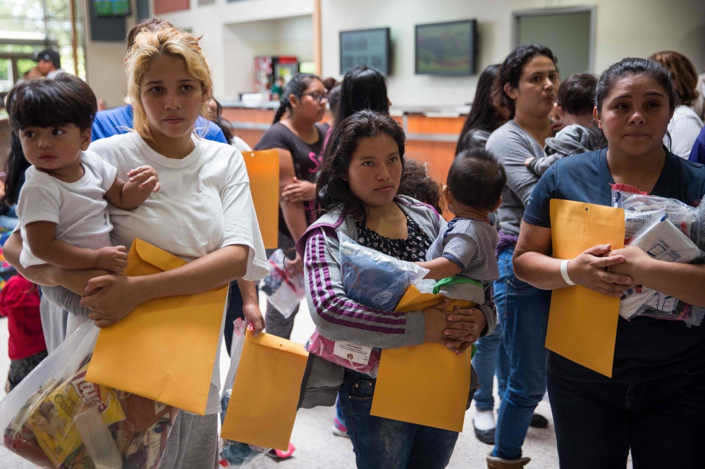 Immigrants wait to head to a nearby Catholic Charities relief center after being dropped off at a bus station shortly after release from detention through 