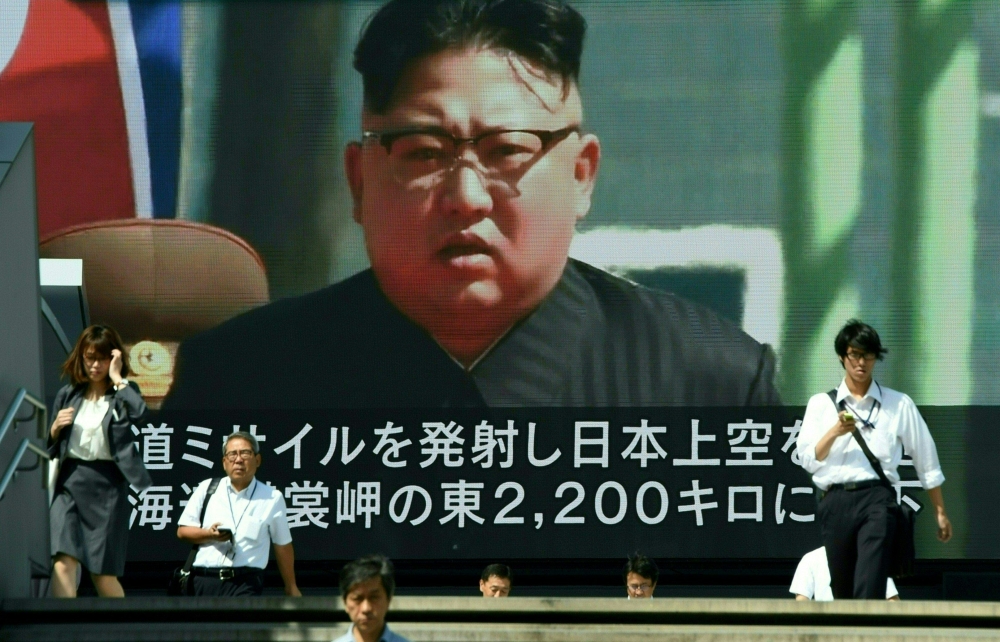 In this file photo taken on September 15, 2017, pedestrians walk in front of a large video screen in Tokyo broadcasting a news report showing North Korean leader Kim Jong-Un, following a North Korean missile test that passed over Japan. / AFP / Toru YAMAN