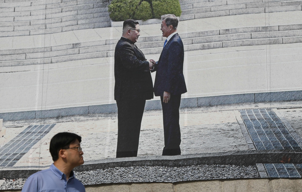 A man walks past a giant banner showing a picture of the summit handshake between South Korean President Moon Jae-in and North Korean leader Kim Jong Un, at Seoul City Hall on September 13, 2018. AFP / Jung Yeon-je