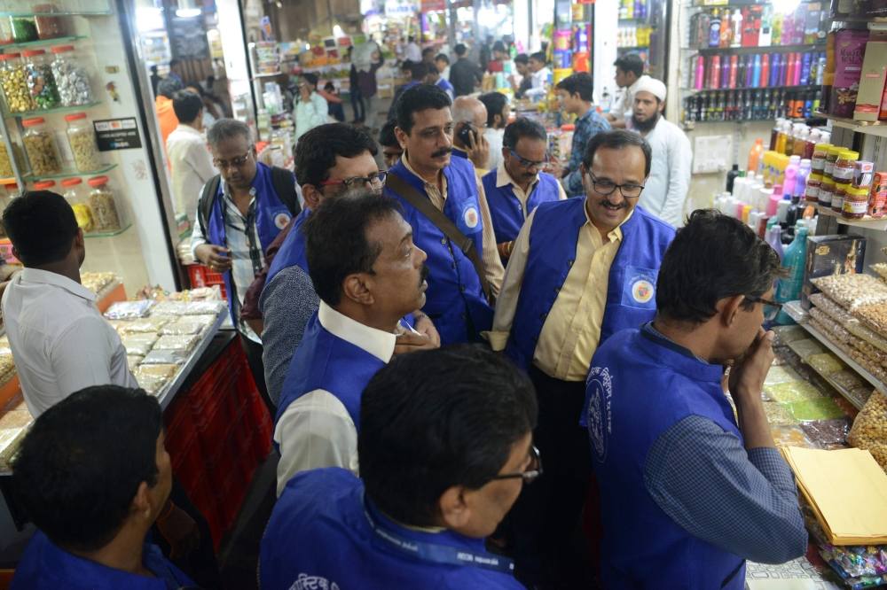 This photograph taken on September 27, 2018 shows city civic officers (in blue) during their visit to a wholesale market to inspect plastic bags usage in Mumbai. AFP / Punit PARANJPE 