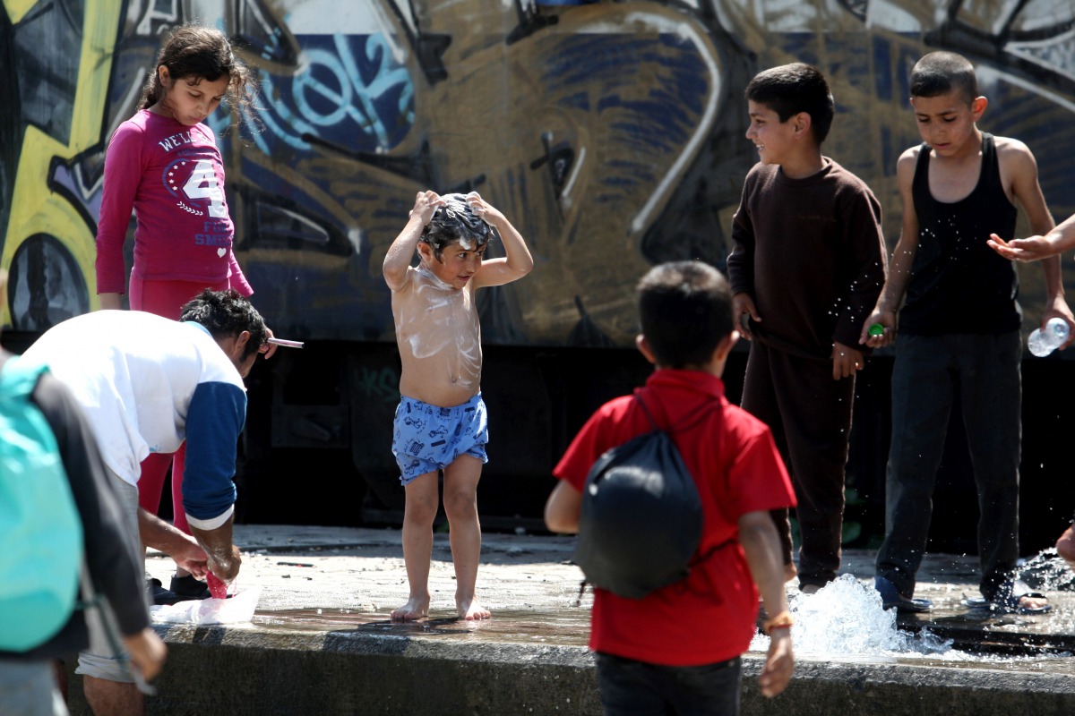 A child washes himself next to a watering hole in the refugees camp at the Greek-FYR of Macedonia border near the village of Idomeni on May 23, 2016. AFP/Sakis Mitrolidis