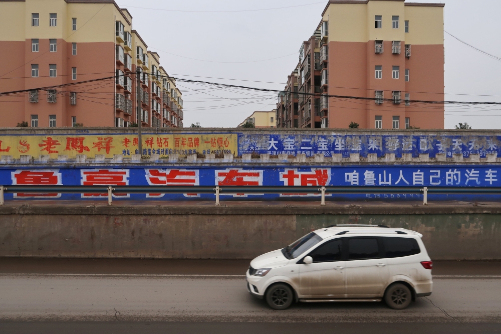 A car moves past a residential area separated by a wall carrying an advertisement of a local auto dealer, in Lushan county, Pingdingshan, Henan province, China November 16, 2018. Reuters/Yilei Sun