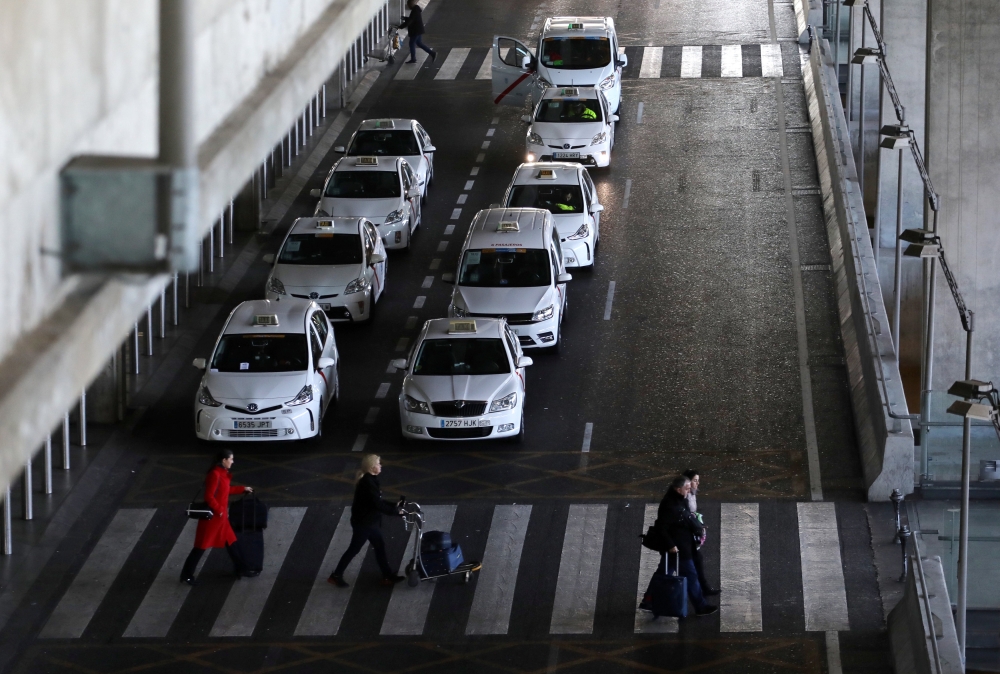 People carry their belongings past parked taxis during an open-end strike against VTC regulations outside Terminal 4 at Adolfo Suarez Barajas airport in Madrid, Spain, January 21, 2019. Reuters/Sergio Perez