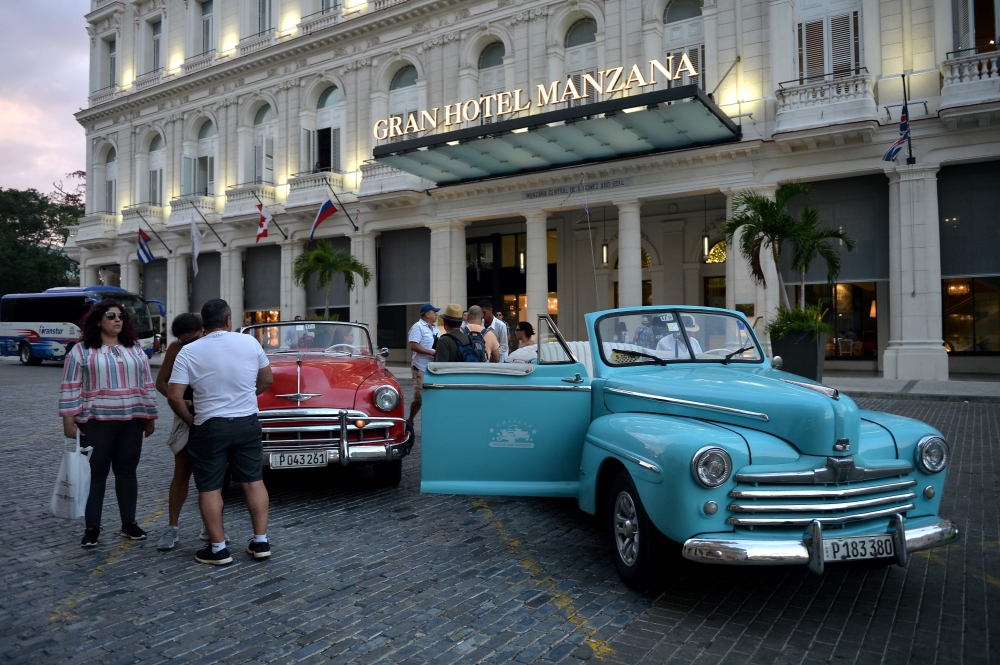 Tourists stand next to an old American car in front of the Gran Manzana Hotel in Havana, on February 11, 2019.  AFP / Yamil Lage 